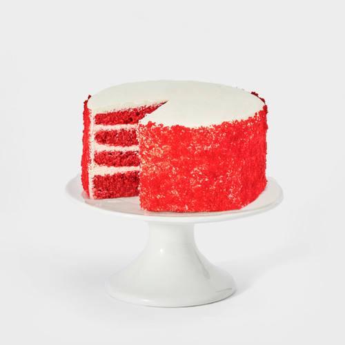 Red Velvet cake on a white background with a slice removed so you can see the inside of the cake showing off the 4-layers of red velvet cake and cream cheese frosting. You can also see the colorful confetti sprinkled on top of the cake in this image.